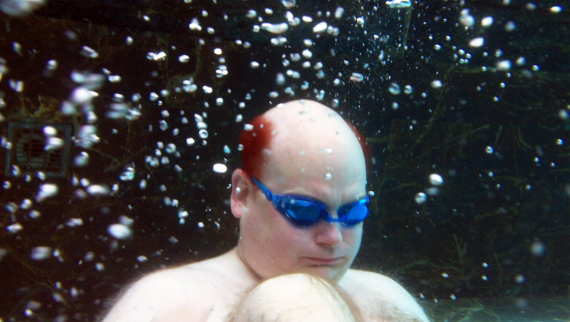 white man with blue goggles and red hair hovers closed up amid a field of bubbles